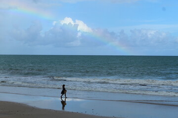 mulher na praia de boa viagem, recife, pernambuco, com arco-&iacute;ris no c&eacute;u 