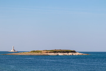 Scenic view of white lighthouse Porer seen from Cape Kamenjak National Park near Premantura, Istria, Croatia. Island Fenoliga in calm waters of the Adriatic Mediterranean Sea in summer. Seascape