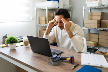 Entrepreneur feeling overwhelmed and dealing with a strong headache while managing an online store...