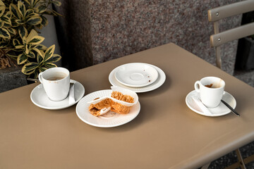 Empty coffee cups and a dessert wrapper are on the table of a coffee shop outside in the city
