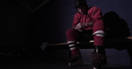 Player lacing up hockey skates in a dark dressing room