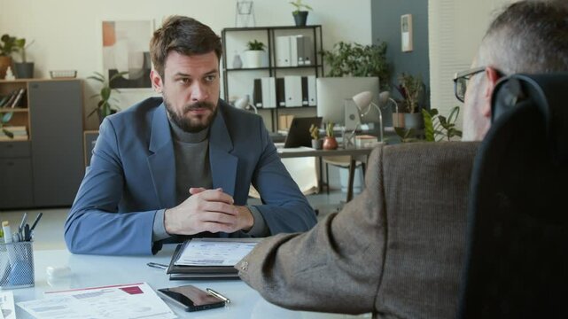 Male employee listening to CEO commenting on his business project, then putting on clown wig and nose while getting fired or pissed off at work in office