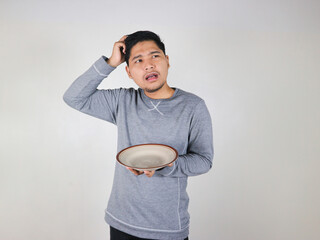 Asian man holding an empty plate with a gesture of thinking hard, hand on head
