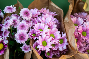 A bunch of pink flowers are in brown paper bags. The flowers are arranged in a way that they are all facing the same direction. The bags are placed on a table