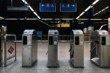 A row of turnstiles are lined up in a station. The turnstiles are silver and have a green arrow on them
