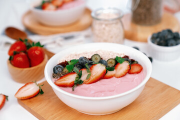Presented by fruits putting yogurt toppings with strawberry, berry, oats, raisins and chia seed decorated by peppermint in white blow. Pink background. Set of healthy dairy product choice. Pecuniary.