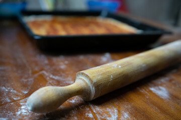 Close up of a rolling pin and a pizza in the background
