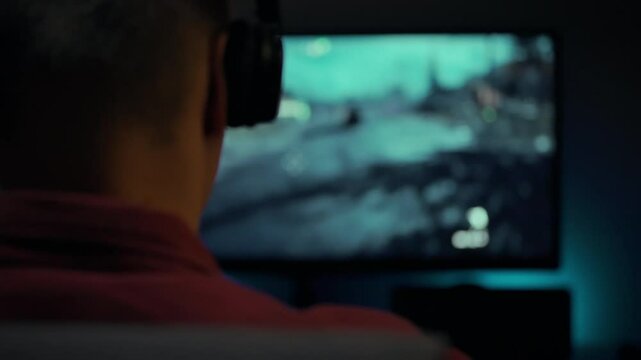 A person wearing headphones is deeply engaged in a thrilling racing game displayed on a large screen. The gaming environment is dimly lit, enhancing focus on the vibrant visuals