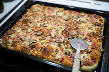 Homemade pizza in a baking sheet with pizza cutter wheel