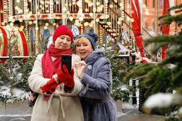 Excited, selfie and group of senior friends in outdoor Christmas market holidays. Diversity, happy and elderly people in retirement taking picture together at illuminated carnival Christmas carousel