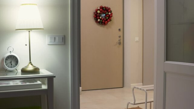 Woman and child return home from a walk. Mother and little boy taking off winter outerwear in hallway of apartment. Front door decorated with Christmas wreath.