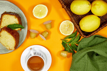 Glass cup with lemon, mint tisane with a bouquet of gypsophila flowers and pound cake on yellow background