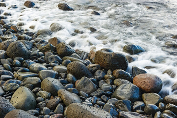 Shallow waves lapping against smooth wet cobblestones on a beach in Maui at sunset