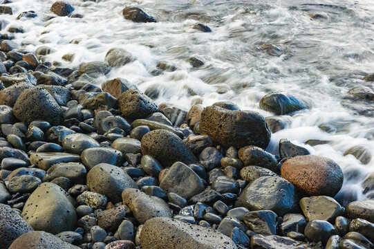 Shallow waves lapping against smooth wet cobblestones on a beach in Maui at sunset