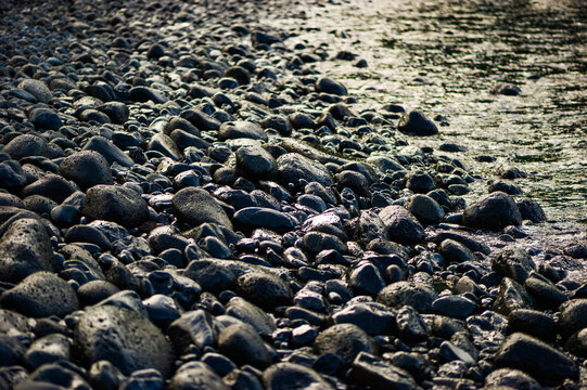 Shallow waves lapping against smooth wet cobblestones on a beach in Maui at sunset