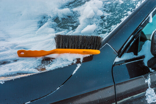 Orange brush removing snow from car windshield in winter