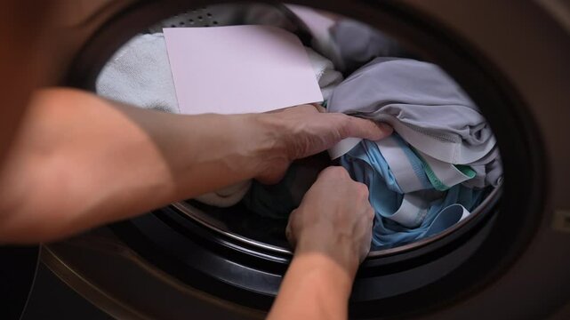 Close-up of housewife man putting pink laundry detergent sheet into washing machine drum, preparing to wash load of clothes, ensuring fresh and clean laundry. Concept of cleanliness and housekeeping.