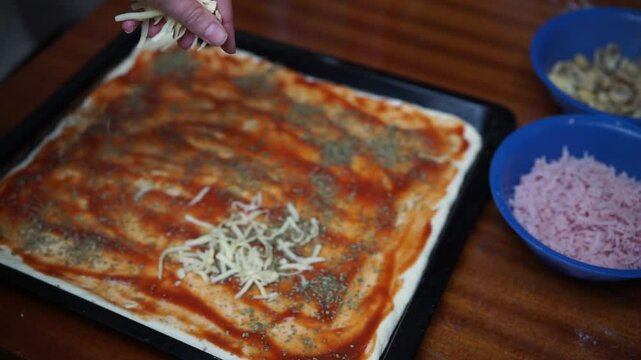 Close up of woman's hand adding cheese on pizza dough