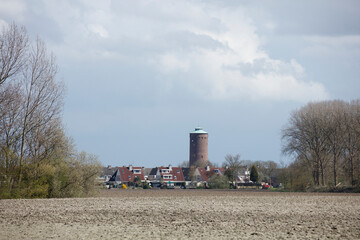 Fototapeta premium Rural Dutch landscape with houses, water tower, and plowed field. Cloudy spring day.