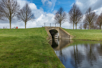 Obraz premium Canal lock with arched bridge, surrounded by grassy banks and bare trees. Springtime scene.