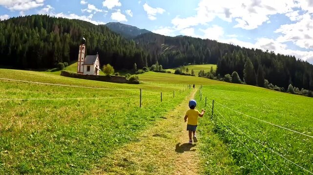 Child enjoying the idyllic landscape of st. Magdalena church and the odle mountains in val di funes