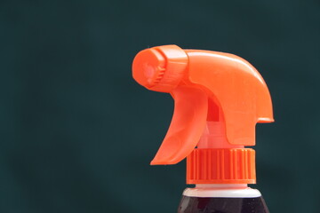 Orange color plastic spray bottle. Water sprayer. Dark green background. House-cleaning concept photo.