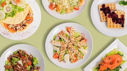 Food assortment on olive background. Chicken caesar salad, Caesar salad, beef salad, waffles, smoked salmon salad, Omelette with tomatoes and mushrooms