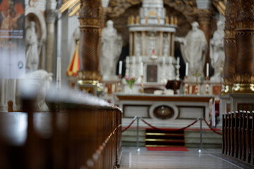 Blurred interior of a church, showing altar, pews, and statues.  A red rope barrier is visible.  Religious atmosphere.