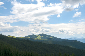 Stunning mountain landscape with lush green hills and dense forests under a bright blue sky filled...