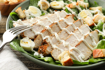 Delicious Caesar salad with chicken on wooden table, closeup