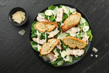 Delicious Caesar salad with chicken and cheese on black textured table, flat lay