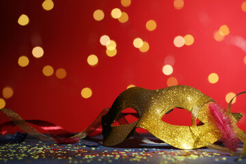 Beautiful carnival mask, ribbons and confetti on color background with blurred lights, closeup