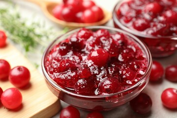 Tasty cranberry sauce in glass bowl and berries on table, closeup