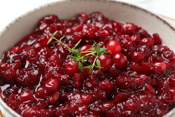 Tasty cranberry sauce and thyme in bowl, closeup