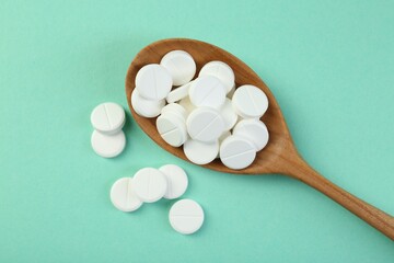 Antibiotic pills in spoon on turquoise background, top view