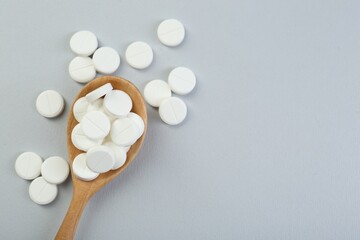 Antibiotic pills in wooden spoon on grey background, top view. Space for text