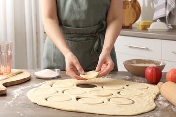 Woman making pirozhki (stuffed pastry pies) at wooden table indoors, closeup