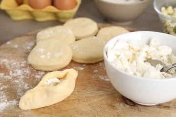 Making pirozhki (stuffed pastry pies). Pieces of dough with cottage cheese on wooden table, closeup