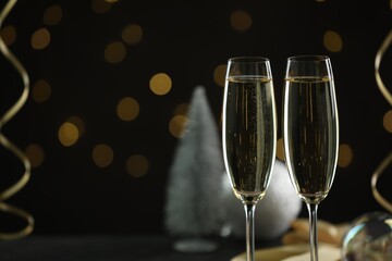 Delicious champagne in glasses and Christmas decor against black background with blurred lights, closeup. Space for text