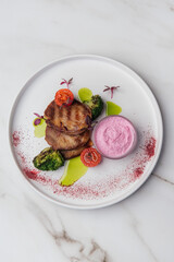 Slices of grilled beef tongue are served with horseradish sauce, broccoli, cherry tomatoes, and microgreens, creating a flavorful dish on a white plate. Restaurant or cafe menu, cookbook recipe
