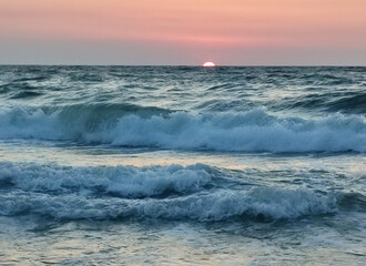 Stormy sea. Big waves with white foam on sea on backdrop of sunset and dawn. Blue sea with orange red sky and sun. Coast seashore seaside sea shore coastline. Natural background nature backdrop storm