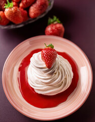 A swirl of whipped cream topped with fresh strawberries is served on a pink ceramic plate with a red berry sauce.