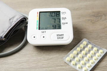 Blood pressure measuring device and pills on wooden table, closeup