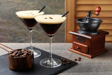 Glasses of delicious espresso martini, manual coffee grinder and beans on wooden table