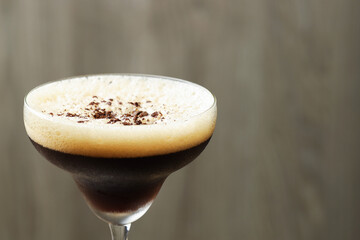 Delicious espresso martini with coffee beans in glass on blurred background, closeup. Space for text