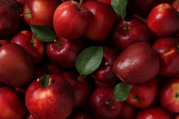 Fresh ripe red apples and green leaves as background, top view