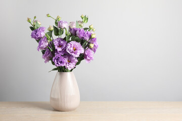 Vase with beautiful eustoma flowers on wooden table, space for text