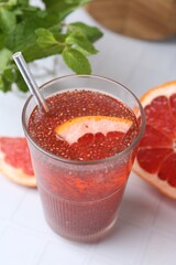 Glass of drink with chia seeds and grapefruit on white tiled table, closeup