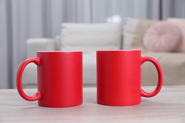 Blank red ceramic mugs on white wooden table. Mockup for design