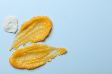 Smears of body scrubs on light blue background, flat lay. Space for text